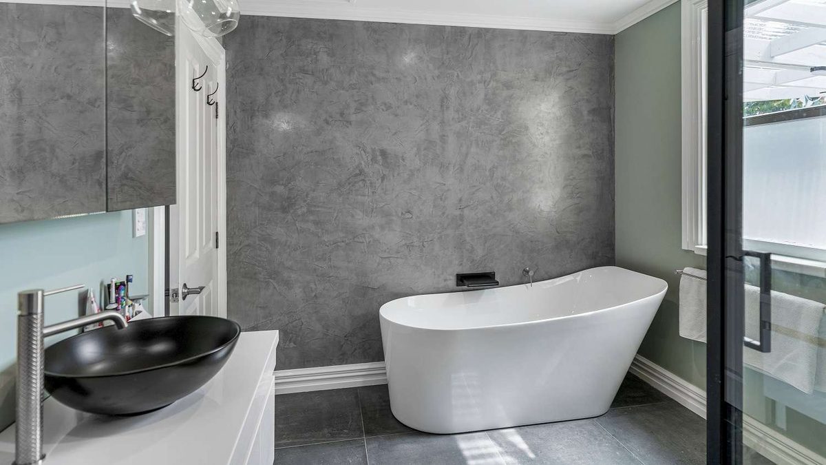 A bathroom with a grey concrete-look feature wall, a freestanding white bath and a black vessel basin
