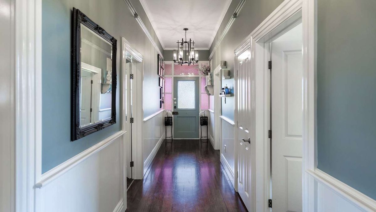 The same villa hallway after painting, with pale blue-grey walls above a white dado rail, white doors and a dark timber floor