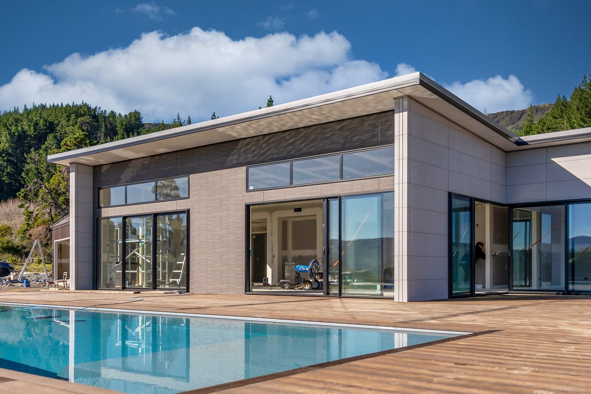 A modern single-storey house with large sliding glass doors behind a swimming pool and a timber deck