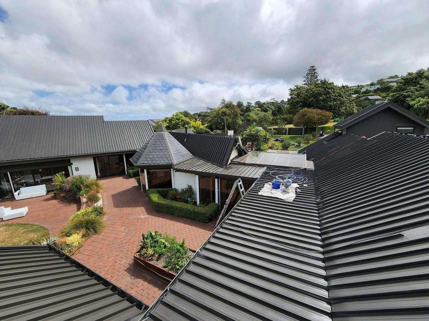 Dark grey metal roofs of a group of houses seen from above, with a brick courtyard and gardens between them
